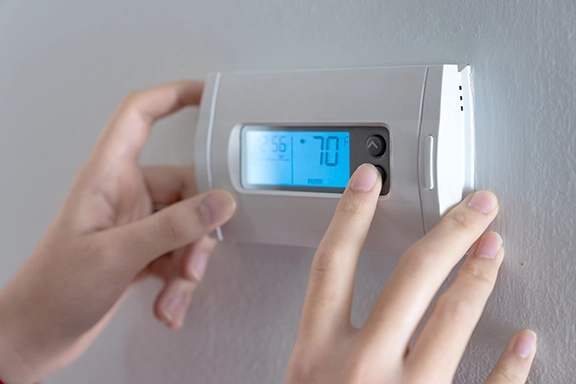 Person adjusting a digital thermostat displaying a temperature setting of 70 degrees, emphasizing HVAC efficiency and comfort during colder months.