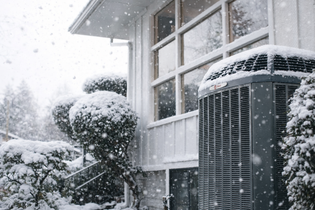 Heat pump covered in snow outside a home during winter, emphasizing HVAC system performance in cold weather.